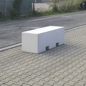 Lichtgrijs betonnen afzetblok van 820 kg met lepelgaten, staand op straatstenen.