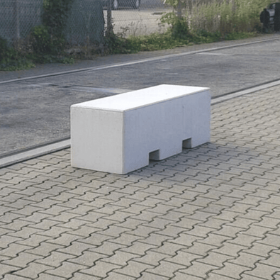 Lichtgrijs betonnen afzetblok van 820 kg met lepelgaten, staand op straatstenen.