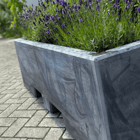 Antraciet afzetblok/bloembak met lepelgaten, gevuld met lavendel, op een stenen terras.