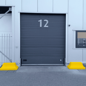 Twee gele betonnen afzetblokken van 330 kg met hijspunt voor een magazijndeur.
