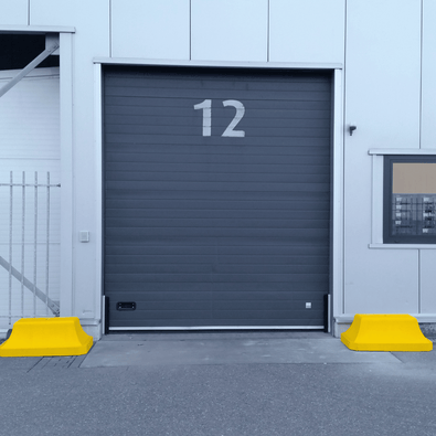 Twee gele betonnen afzetblokken van 330 kg met hijspunt voor een magazijndeur.