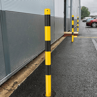 Gele en zwarte afzetpaal Ø60 mm, staand op asfalt naast een gebouw.
