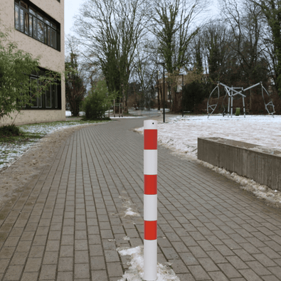 Wit-rode afzetpaal Ø76 mm op een bestraat pad met sneeuw, geschikt voor verankering.