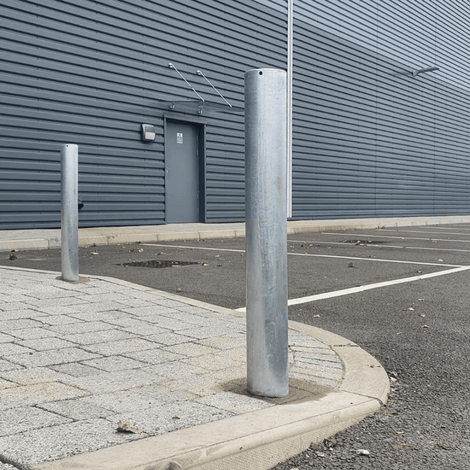 Verzinkte stalen afzetpaal Ø89 mm, verankerd in beton, met een kleinere paal op de achtergrond.