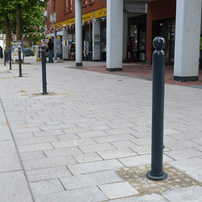 Donkergrijze design afzetpaal Ø76 mm met kogelkop op een trottoir, voor verkeersregulatie.