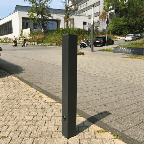 Zwarte design afzetpaal, 80x80 mm met vlakke kop, staand op een grijze tegelstoep.