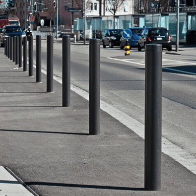 Donkergrijze design afzetpalen (Ø82 mm) met vlakke kop langs een stedelijke weg.