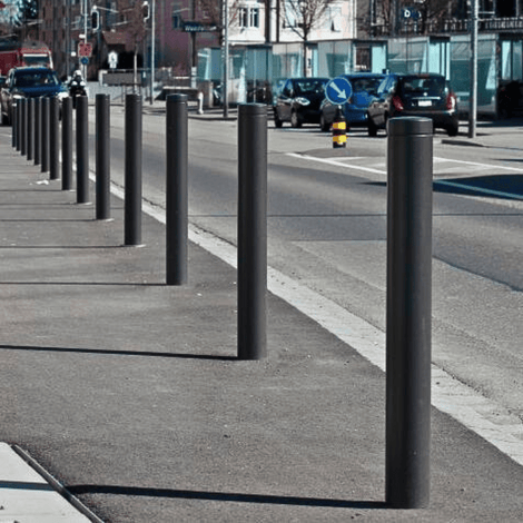 Donkergrijze design afzetpalen (Ø82 mm) met vlakke kop langs een stedelijke weg.