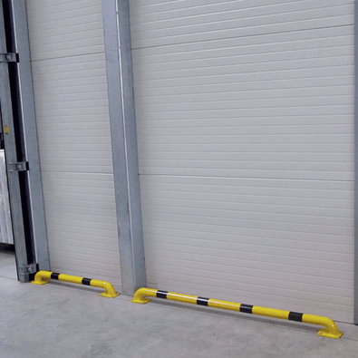 Gele en zwart gestreepte stootbeschermer Ø60 mm op voetplaat, gemonteerd voor een witte garagedeur.