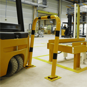 Gele en zwart gestreepte beschermbeugel Ø76 mm op flexibele voetplaat, naast een heftruck in een magazijn.