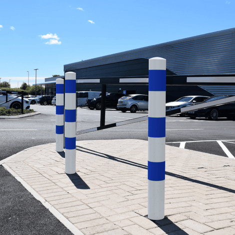 Witte en blauwe beschermpalen (Ø102 mm) op een parkeerplaats, geschikt voor betonverankering.