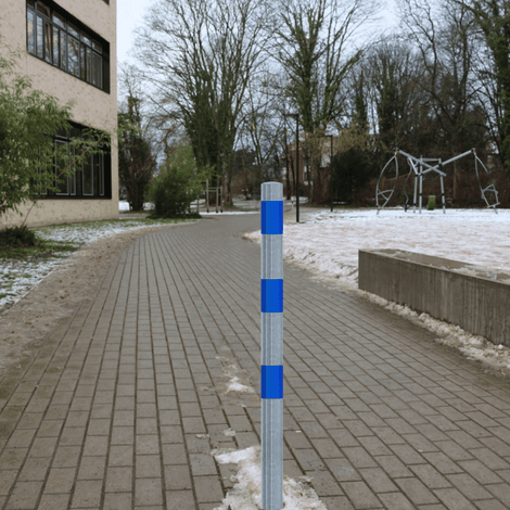 Verzinkt-blauwe beschermpaal Ø60 mm met blauwe reflecterende strepen, staand op een bestraat pad.