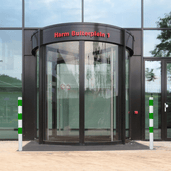 Twee wit-groene beschermpalen Ø60 mm voor betonverankering bij een glazen draaideur.