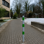 Verzinkt-groene beschermpaal Ø60 mm op een bestraat pad met sneeuw, ideaal voor betonverankering.