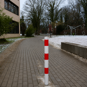 Witte en rood gestreepte beschermpaal Ø76 mm op een bestrate weg met sneeuw.