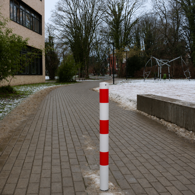 Witte en rood gestreepte beschermpaal Ø76 mm op een bestrate weg met sneeuw.
