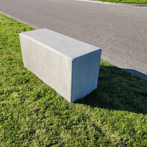 Antraciet betonnen poef, 1000x400x500 mm, rechthoekig, op groen gras naast een pad.
