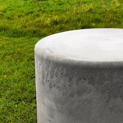 Antraciet betonnen poef, Ø450x950 mm, met ruwe textuur, staand in groen gras.
