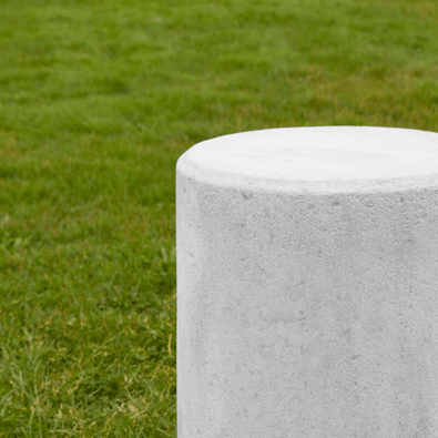 Grijze betonnen poef, Ø450x950 mm, met gladde afwerking, staand op groen gras.