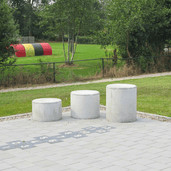 Drie ronde, grijze betonnen poefs in verschillende hoogtes op een tegelpad met hinkelbaan.