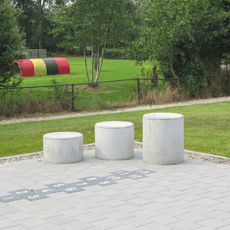 Drie ronde, grijze betonnen poefs in verschillende hoogtes op een tegelpad met hinkelbaan.