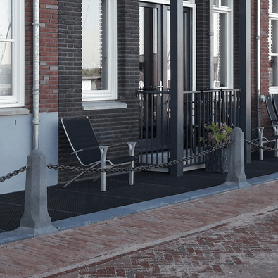 Achthoekige betonnen sierpaal in grijs, met ketting, voor afbakening van terras.