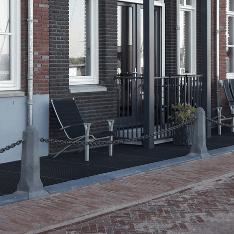 Achthoekige betonnen sierpaal in grijs, met ketting, voor afbakening van terras.