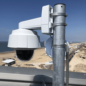 Verzinkt stalen dakmast met witte beveiligingscamera, gemonteerd op een dak met strandzicht.