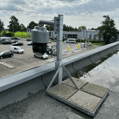 Verzinkt stalen dakmast met tegelvoet, ondersteunt een grijze camera op een plat dak.