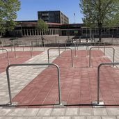 Verzinkt stalen fietsbeugels (Ø48 mm) met betonvoeten, geplaatst op rode en grijze tegels.