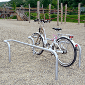 Verzinkt stalen fietsbeugel met gebogen hoek, buis Ø42 mm, met een witte fiets op een grindplein.