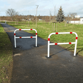 Twee wit-rode fietssluis hekken van Ø60 mm op een fietspad, verankerd in beton.