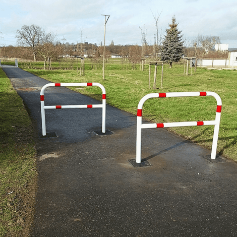 Twee wit-rode fietssluis hekken van Ø60 mm op een fietspad, verankerd in beton.