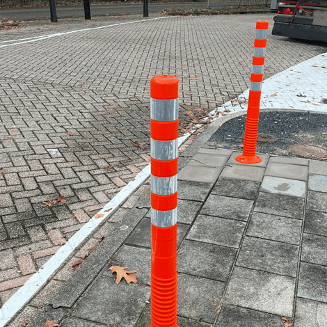 Oranje-witte flexibele paaltjes met reflecterende banden op een stoep.