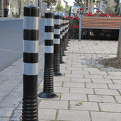 Zwart-witte flexibele afzetpalen met reflecterende strepen op een trottoir.