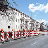 Rood-wit gestreepte geleidebakens met oranje knipperlichten langs een weg met gebouwen.