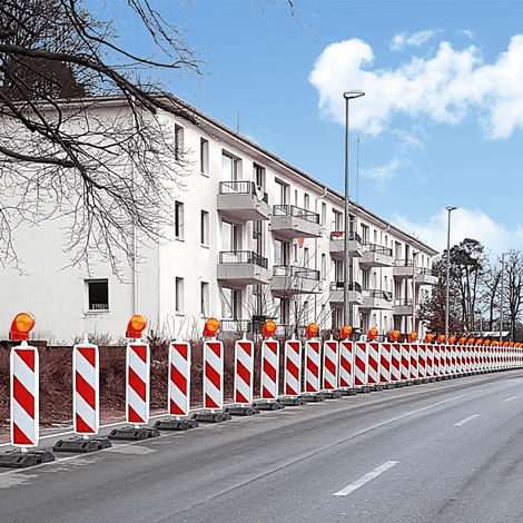 Rood-wit gestreepte geleidebakens met oranje knipperlichten langs een weg met gebouwen.