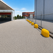 Gele betonnen jumboblokken van 330 kg langs een hekwerk als aanrijdbeveiliging op een industrieterrein.