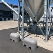 Twee grijze Jumboblokken van Oud Hollands stampbeton met lepelgaten, liggend onder een grote silo.