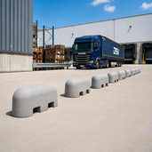 Grijze jumboblokken van 310 kg met lepelgaten van Oud Hollands stampbeton toegepast als aanrijdbeveiliging bij een laad- en losperron van een distributiecentrum.