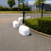 Witte betonnen jumboblokken van 330 kg geplaatst als aanrijdbeveiliging en terreinafbakening bij een toegangshek van een bedrijventerrein.
