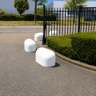 Witte betonnen jumboblokken van 330 kg geplaatst als aanrijdbeveiliging en terreinafbakening bij een toegangshek van een bedrijventerrein.