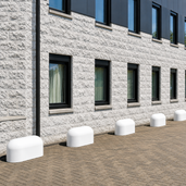 Witte betonnen jumboblokken van 330 kg in oud Hollands stampbeton geplaatst als aanrijdbeveiliging langs de gevel van een modern bedrijfsgebouw.