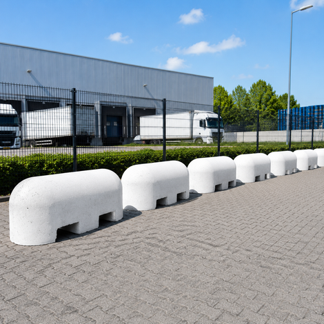 Witte betonnen jumboblokken met lepelgaten geplaatst als aanrijdbeveiliging en terreinafscheiding op een industrieterrein.