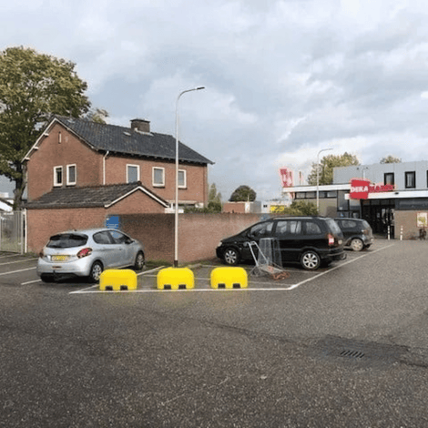 Drie gele Jumboblokken van Oud Hollands stampbeton met lepelgaten, gebruikt als parkeerbegrenzers.