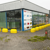 Rij gele Jumboblokken van Oud Hollands stampbeton met hijsoog, langs een bedrijfsgebouw.