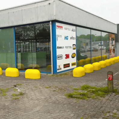 Rij gele Jumboblokken van Oud Hollands stampbeton met hijsoog, langs een bedrijfsgebouw.