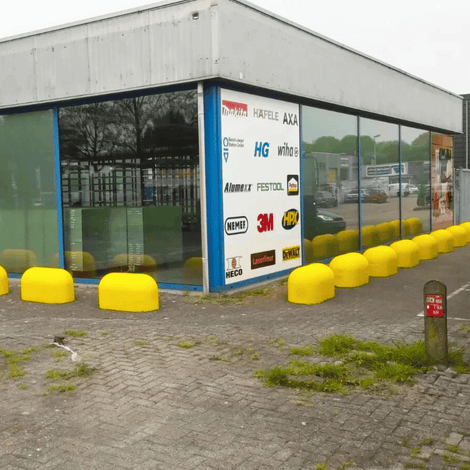 Rij gele Jumboblokken van Oud Hollands stampbeton met hijsoog, langs een bedrijfsgebouw.