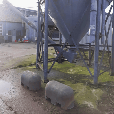 Twee grijze Jumboblokken van Oud Hollands stampbeton met lepelgaten, liggend onder een grote silo.