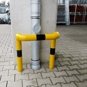Gele en zwarte stalen kolombeschermer Ø76 mm met 2x 90° hoeken, verankerd in beton.
